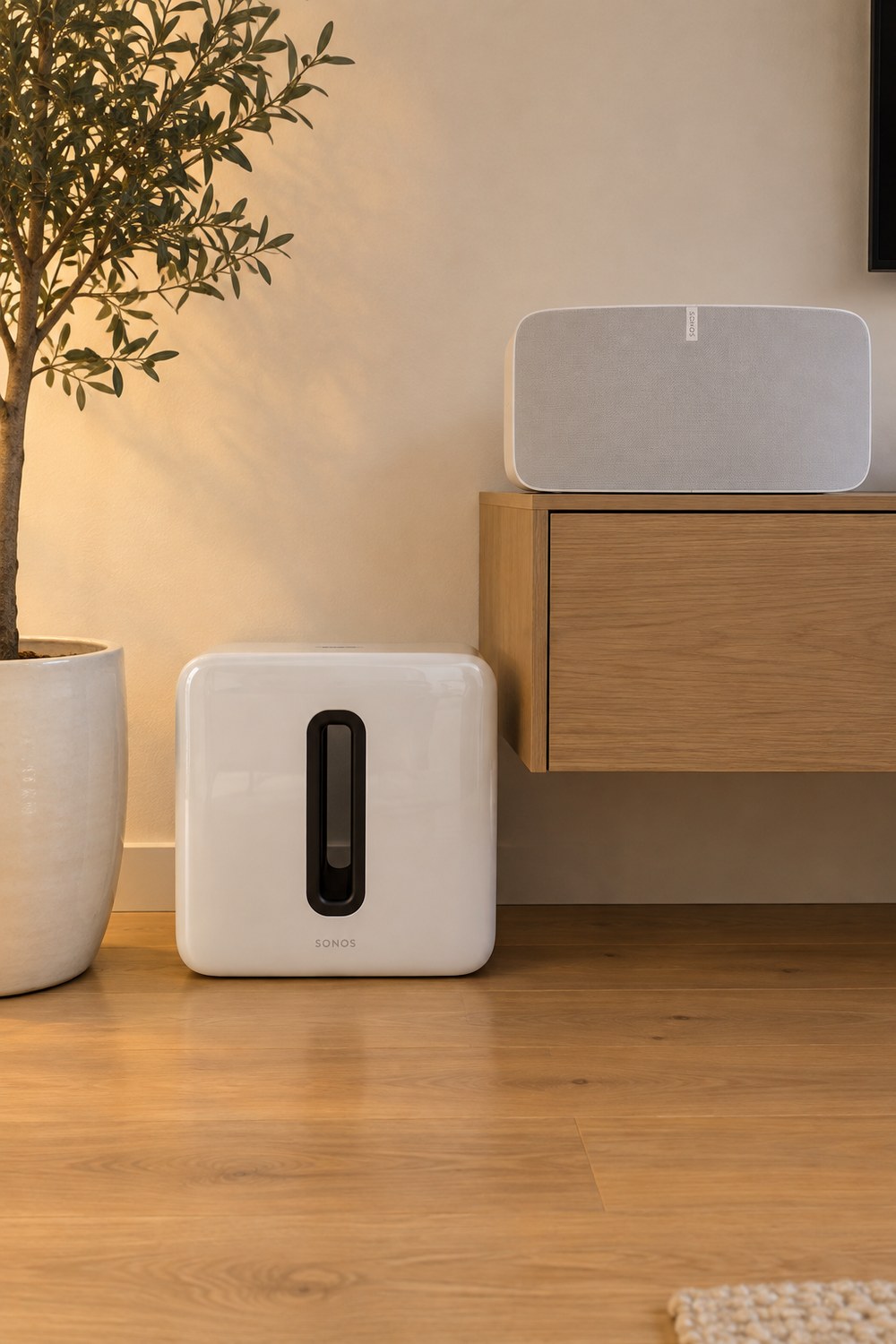 Weißer Sonos Sub 4 in Hochglanz mit der Öffnung in der Mitte am Boden neben dem Lowboard, darüber ein Sonos Five